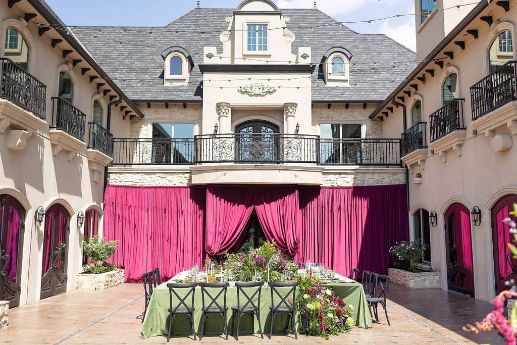 a mansion wedding venue's courtyard. there is red draping and a table decorated with flowers